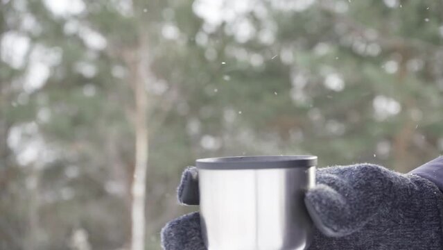 Close-up of a man's hand holding a mug of hot drink from a thermos while standing outside in cold weather