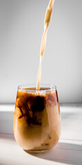iced or frozen coffee in a glass, splash with drops, over grey background