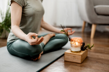 Young relaxed woman doing yoga at home with candles and incense, close-up of hands - obrazy, fototapety, plakaty