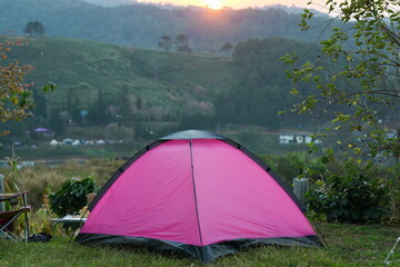 A bright pink travel tent is set in a courtyard with a beautiful morning view of the mountains. Himalayan wild cherry with pink flowers in the distance at sunrise vacation travel ideas
