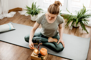 Young relaxed woman doing yoga at home with candles and incense - obrazy, fototapety, plakaty