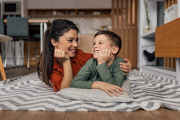 Laughing caucasian single mother, wraping her arm around her son, smiling together.