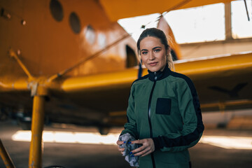 Portrait of confident female pilot in the suit, standing next to an airplane.