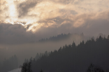 The sun through the  dark clouds. The brightness of the sun forms very different clouds and makes the mountain very mysterious.