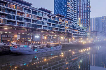 Fototapeta premium Rotterdam, The Netherlands, January 12, 2022: modern residential buildings, partly under construction, and historic vessels reflect in the still water of Wijnhaven harbour on a misty morning