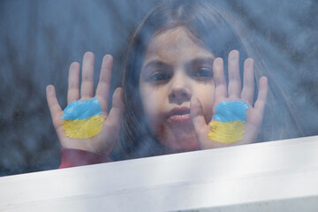 A little girl in the window of her house with a painted yellow-blue flag of Ukraine, peace in Ukraine, stop the war, protest and patriot, home