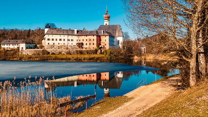 Beautiful winter wonderland with reflections and a monastery at the famous Hoeglwoerther See lake, Bavaria, Germany