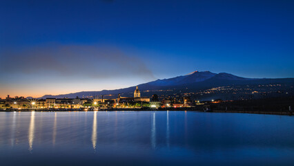 Il vulcano Etna e la citta di Riposto nell'ora blu dopo il tramonto 
