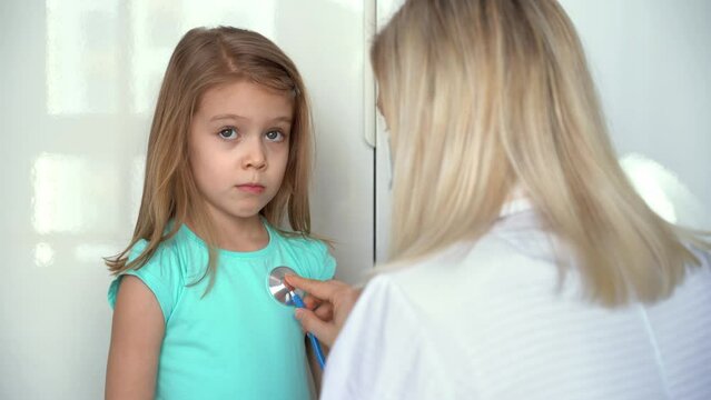 Back View Female Doctor Pediatrician Uses Stethoscope Listen Heart Of Child Girl Patient. Lung Breathing Check. Medicine And Healthcare Concept.