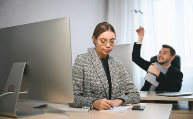 Young attractive woman and adult man are working in the office. A man in the background is playing with a paper airplane. Open space concept for teamwork