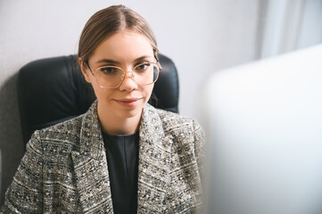 Attractive young woman in glasses working on the computer in the office. Businesswoman in modern office space or coworking open space