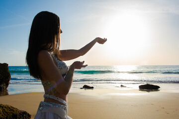 Happy and calm woman poses on the beach wearing the typical belly dance costume. Exotic beauty. Girl silhouette.