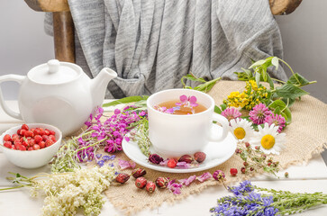 Herbal tea with rosehip, chamomile and clover in a white cup on a wooden table with flowers