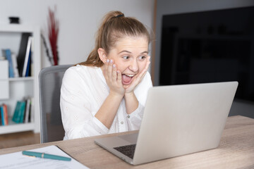 Happy young woman hands on face looking at laptop