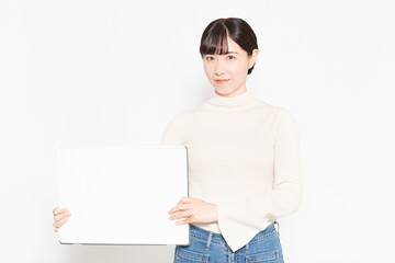 白い壁の前に立って大きなスケッチブックを見せる女性