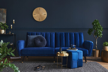 Stylish modern living room interior design with glamour blue sofa, metal shelf, coffee table, pouf and elegant home accessories. Dark blue wall. Home staging. Template. Copy space..