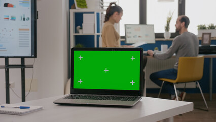 Close up of laptop with green screen on empty office desk. Isolated template and mock up copy space background on computer display with chroma key. Digital mock up app on screen.