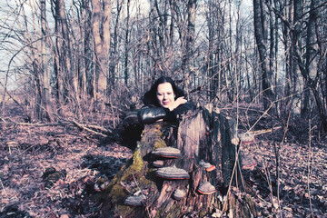 A young woman hides behind a large tree stump in the forest.