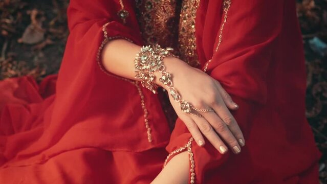 Close-up woman's hands showcase arabic jewelry gold bracelets with stones, luxury royal traditional accessory saudi arabia. Red silk dress. Queen oriental girl fashion model posing, face cropped