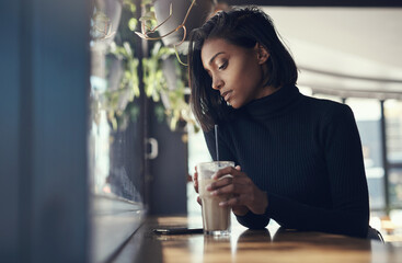 Never keep a good woman waiting. Shot of a beautiful young woman drinking a iced coffee in a cafe.