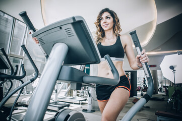 Attractive muscular smiling fitness woman running on treadmill in gym
