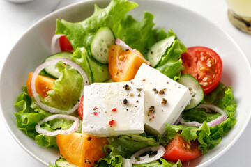 Close up greek salad with feta cheese, onion, tomatoes, cucumber, green lettuce on white plate.