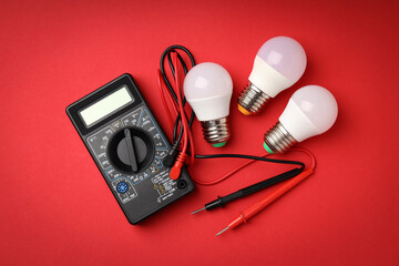 Multimeter and energy saving bulbs on red background