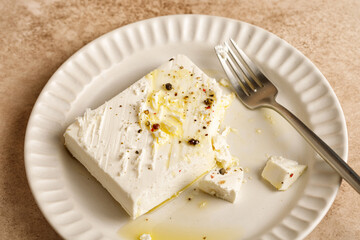 Natural marinated greek feta cheese on white plate with olive oil and herbs, pepper.