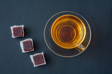 Pieces of fruit marmalade in paper napkins and a cup of tea in a transparent cup on a plate