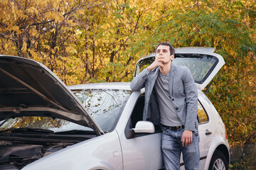 A man looks under the open hood of a car. The car broke down on the road.