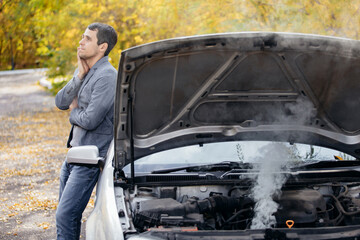 A man looks under the open hood of a car. The car broke down on the road. The engine is smoking