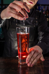 Bartender dressed in black apron and shirt make red cocktail drink on black background