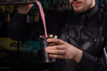 Bartender dressed in black apron and shirt make cocktail drink on black background