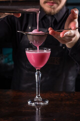Bartender dressed in black apron and shirt make cocktail drink on black background