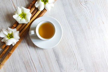 Fototapeta na wymiar Herbal tea in white cup, brown bamboo and white flowers on wooden table with copy space. Top view