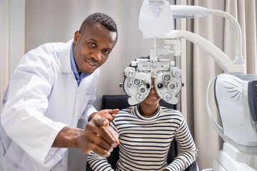 African young woman girl doing eye test checking examination with male man optometrist using phoropter in clinic or optical shop. Eyecare concept. - obrazy, fototapety, plakaty