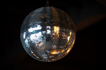 Closeup on shiny disco ball with bright rays against dark background.