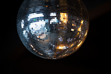 Closeup on shiny disco ball with bright rays against dark background.