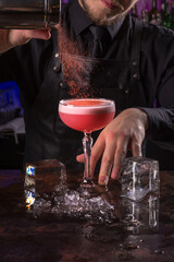 Bartender dressed in black apron and shirt sprinkled with chocolate on a cocktail on black background