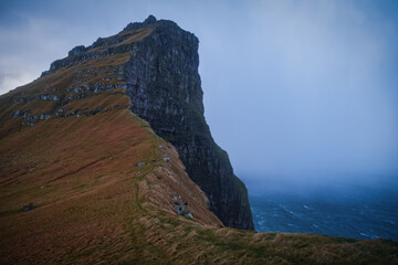 Fototapeta na wymiar Kalsoy Island with Kallur lighthouse on on Faroe islands, Denmark, Europe. Clouds over high cliffs, turquoise Atlantic ocean and spectacular views. November 2021