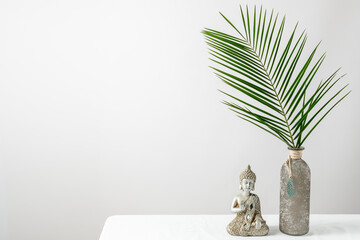 Modern minimal interior floral decoration with natural palm leaves in vintage glass vase and Buddha...