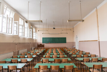 Empty old faculty or college School classroom with row of chairs, green desk tables, chalkboard and big white windows. Natural light.