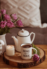 Fototapeta na wymiar Still-life. A vase with flowers, tulips, a teapot, a bunny, a candle and a cup of tea on the coffee table in the living room home interior. Cozy spring concept.