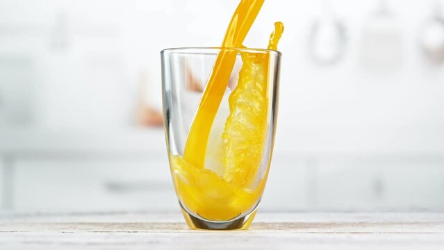 Super slow motion of pouring orange juice into glass. Placed on white table with kitchen interior. Filmed on high speed cinema camera, 1000 fps. Speed ramp effect.
