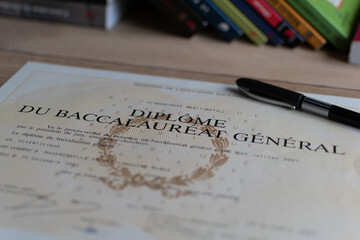 Baccalaureate : close up of a french diploma with some books, the text means general baccalaureate...