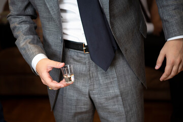 Close up of man in elegant suit with necktie holding glass of brendy (rakija),schnapps at wedding...