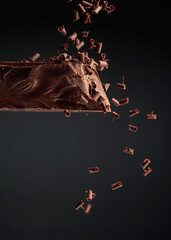 Piece of dark chocolate and falling chocolate crumbs.