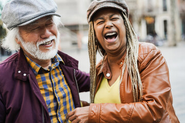 Multiracial senior couple having fun outdoor with city in background - Love, relationship and joyful elderly lifestyle concept - Focus on japanese man face