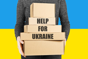 A volunteer holds boxes of humanitarian aid for Ukraine against the background of a blue and yellow flag. Help for refugees.