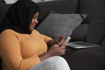 Young muslim woman shopping online and paying with a credit card sitting on the floor.